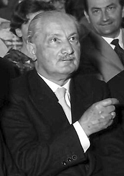 Black-and-white photo of a seated man in a dark suit with white hair